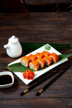 sushi on a plate with chopsticks next to it and a teapot