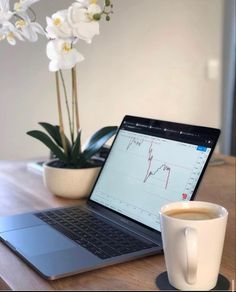 a laptop computer sitting on top of a wooden table next to a cup of coffee