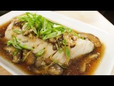 a white plate topped with fish covered in mushrooms and sauce on top of a wooden table