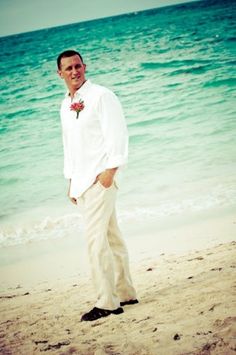 a man standing on top of a sandy beach next to the ocean with his hands in his pockets