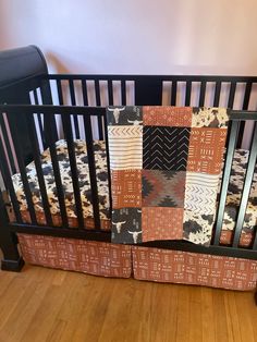 a baby crib with an orange and black quilt on the bedding, next to a wooden floor