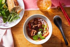 a bowl of beef and noodle soup on a wooden table