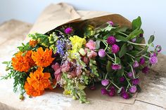 a bunch of flowers sitting on top of a wooden table next to a brown paper bag