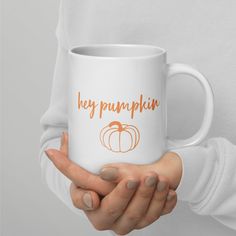 a woman holding a white coffee mug with the words hey pumpkin on it in orange lettering