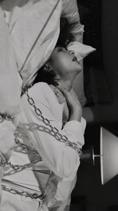 a black and white photo of a woman with chains around her neck wearing a hat