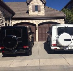 two jeeps parked in front of a house with garage doors open and one is white