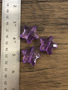 three pieces of purple glass sitting on top of a wooden table next to a ruler