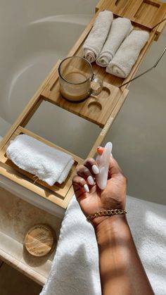 a person holding an item in their hand near a bathtub with towels on it