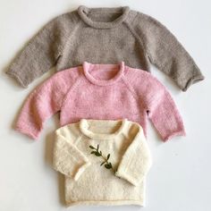 three sweaters are laid out on a white surface, one is pink and the other is grey