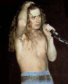 a man with long hair and no shirt on holding a microphone in his right hand