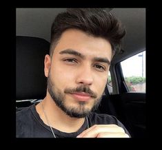 a young man with a beard is sitting in the back seat of a car and looking at the camera