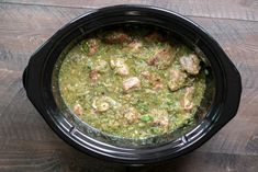 a black crock pot filled with meat and green sauce on top of a wooden table