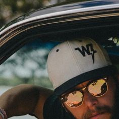 a man wearing sunglasses and a hat sitting in a car with his head out the window