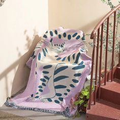 a cat laying on top of a blanket next to a stair case and potted plant