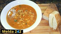 a white bowl filled with soup next to a piece of bread on a cutting board