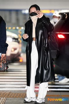 a woman in black coat and white pants walking down the street with her hand on her face