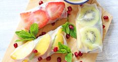 fruit wrapped in plastic sitting on top of a cutting board next to a bowl of yogurt