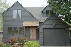 a gray house with two garages and flowers in the front yard on a sunny day