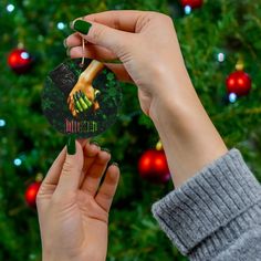 two hands holding up a christmas ornament in front of a tree