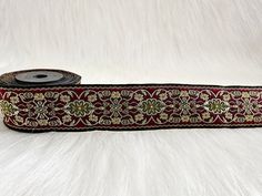 a roll of red and gold ribbon with floral designs on it, sitting on a white furnishing