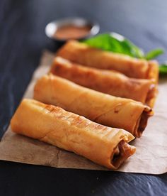 three spring rolls sitting on top of a piece of wax paper next to some dipping sauce