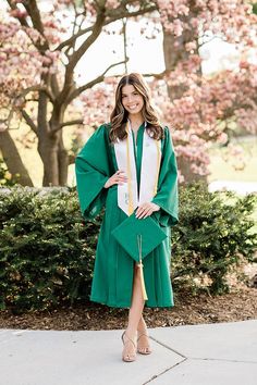 a woman wearing a green graduation gown standing in front of trees