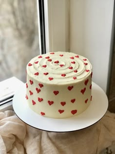 a white cake with red hearts on it sitting on a plate next to a window