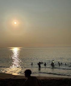 people swimming in the ocean at sunset on a beach with sun reflecting off the water