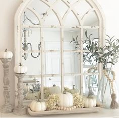 an old window is decorated with white pumpkins and greenery in front of a mirror