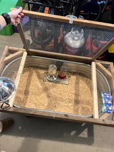 a person holding an open bird cage filled with sand and other items in front of them