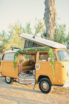 an old vw van is parked in the dirt with its doors open and plants growing on top