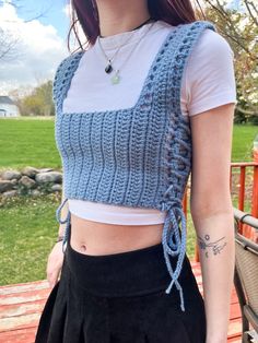 a woman wearing a blue crochet top and black skirt standing on a wooden deck