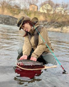 a woman kneeling down in the water with a fish net and fishing pole on her feet