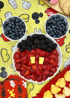 a mickey mouse face made out of berries and blueberries in front of other snacks