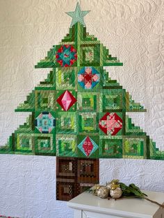 a quilted christmas tree is hanging on the wall next to a white dresser and table