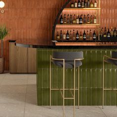 a bar with two stools and several bottles on the wall behind it, along with a potted plant