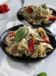 two black plates filled with pasta and veggies on top of a white table