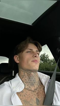 a man with tattoos on his neck and chest sitting in the back seat of a car