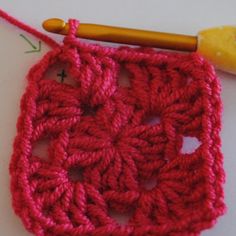 the crochet square is being worked on with a wooden knitting needle and thread