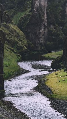 a river running through a lush green hillside covered in grass next to a tall rock formation