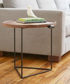 a bird sitting on top of a wooden table next to a gray couch in a living room