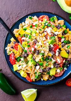 a bowl filled with pasta salad next to sliced avocado and lime wedges