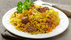 a white plate topped with rice covered in meat and veggies next to a fork