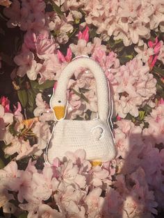 a crocheted swan purse sitting in the middle of pink flowered branches with white flowers