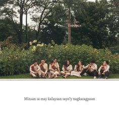 a group of people sitting on top of a lush green field next to trees and bushes