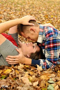 a man and woman laying on the ground covered in leaves with their heads touching each other