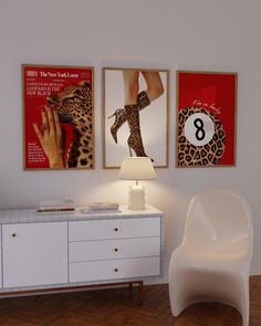 a white chair sitting next to a table with a lamp on it and posters above it