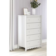 a white chest of drawers in a room with purple walls and wooden floors, along with a vase filled with flowers