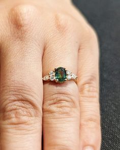 a woman's hand with a green and white diamond ring on top of it