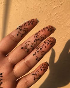 a person's hand with tattoos on their fingers and the shadow of a wall behind them